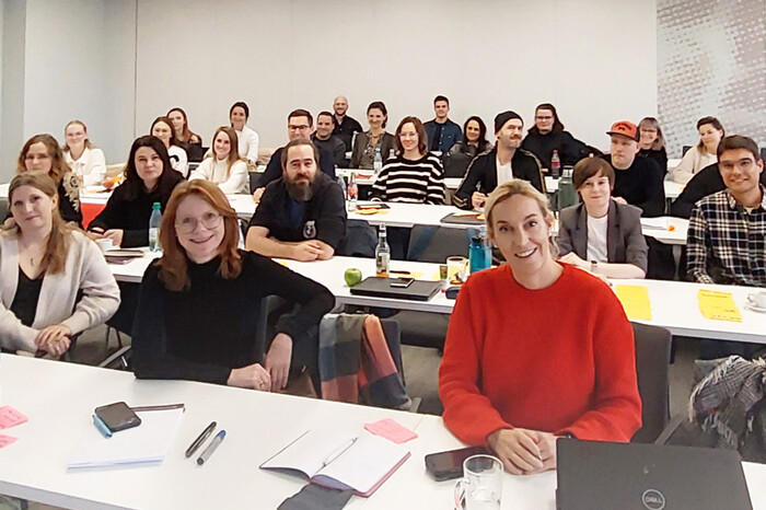Gruppe junger Menschen sitzt im Schulungsraum, Kamera blickt frontal